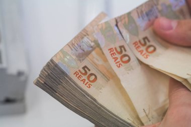 Değişim bürosu / bankada çalışan iş adamının insan eli. O para sayıyor ve bir müşteriye nakit para veriyor. Brezilyalı 50 reais fatura.