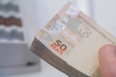 Değişim bürosu / bankada çalışan iş adamının insan eli. O para sayıyor ve bir müşteriye nakit para veriyor. Brezilyalı 50 reais fatura.
