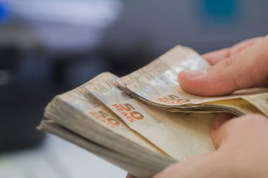 Değişim bürosu / bankada çalışan iş adamının insan eli. O para sayıyor ve bir müşteriye nakit para veriyor. Brezilyalı 50 reais fatura.