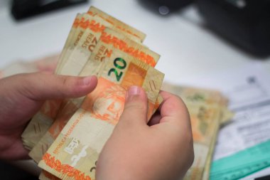 Değişim bürosu / bankada çalışan iş adamının insan eli. O para sayıyor ve bir müşteriye nakit para veriyor. Brezilya Reais - 20 reais fatura.