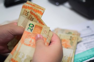 Değişim bürosu / bankada çalışan iş adamının insan eli. O para sayıyor ve bir müşteriye nakit para veriyor. Brezilya Reais - 20 reais fatura.