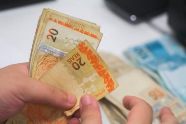 Değişim bürosu / bankada çalışan iş adamının insan eli. O para sayıyor ve bir müşteriye nakit para veriyor. Brezilya Reais - 20 reais fatura.