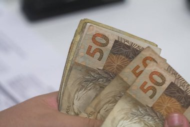 Değişim bürosu / bankada çalışan iş adamının insan eli. O para sayıyor ve bir müşteriye nakit para veriyor. Brezilyalı 50 reais fatura.