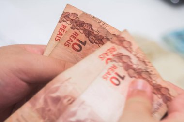 Değişim bürosu / bankada çalışan iş adamının insan eli. O para sayıyor ve bir müşteriye nakit para veriyor. Brezilya Reais - 10 reais fatura.