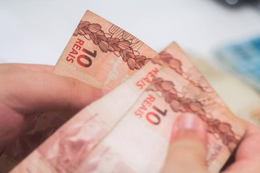 Değişim bürosu / bankada çalışan iş adamının insan eli. O para sayıyor ve bir müşteriye nakit para veriyor. Brezilya Reais - 10 reais fatura.