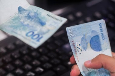 Değişim bürosu / bankada çalışan iş adamının insan eli. O para sayıyor ve bir müşteriye nakit para veriyor. Brezilya Reais 100 reais.