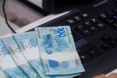 Değişim bürosu / bankada çalışan iş adamının insan eli. O para sayıyor ve bir müşteriye nakit para veriyor. Brezilya Reais 100 reais.