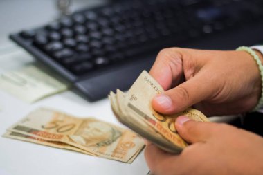 Değişim bürosu / bankada çalışan iş adamının insan eli. O para sayıyor ve bir müşteriye nakit para veriyor. Brezilyalı 50 reais fatura.