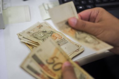 Değişim bürosu / bankada çalışan iş adamının insan eli. O para sayıyor ve bir müşteriye nakit para veriyor. Brezilyalı 50 reais fatura.