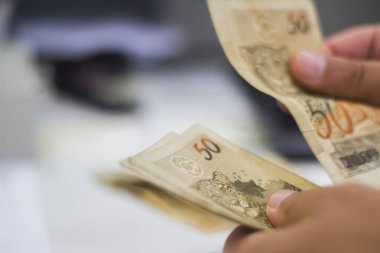 Değişim bürosu / bankada çalışan iş adamının insan eli. O para sayıyor ve bir müşteriye nakit para veriyor. Brezilyalı 50 reais fatura.