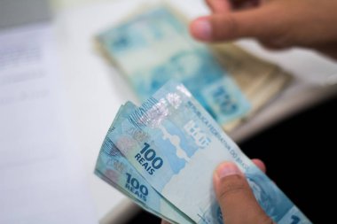 Değişim bürosu / bankada çalışan iş adamının insan eli. O para sayıyor ve bir müşteriye nakit para veriyor. Brezilya Reais 100 reais.