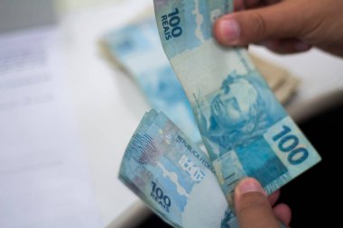 Değişim bürosu / bankada çalışan iş adamının insan eli. O para sayıyor ve bir müşteriye nakit para veriyor. Brezilya Reais 100 reais.