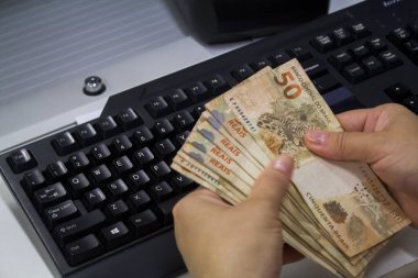 Değişim bürosu / bankada çalışan iş adamının insan eli. O para sayıyor ve bir müşteriye nakit para veriyor. Brezilyalı 50 reais fatura.