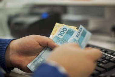Değişim bürosu / bankada çalışan iş adamının insan eli. O para sayıyor ve bir müşteriye nakit para veriyor. Brezilya Reais 100 reais.