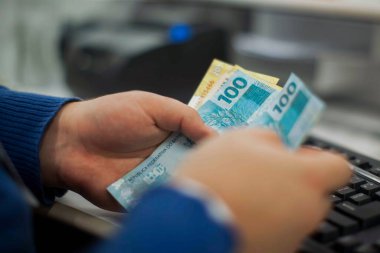 Değişim bürosu / bankada çalışan iş adamının insan eli. O para sayıyor ve bir müşteriye nakit para veriyor. Brezilya Reais 100 reais.