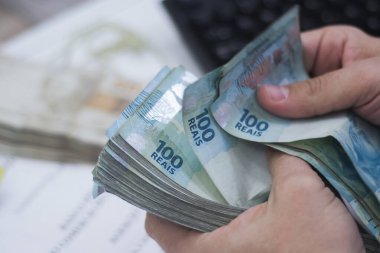 Değişim bürosu / bankada çalışan iş adamının insan eli. O para sayıyor ve bir müşteriye nakit para veriyor. Brezilya Reais 100 reais.