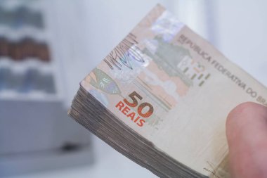 Değişim bürosu / bankada çalışan iş adamının insan eli. O para sayıyor ve bir müşteriye nakit para veriyor. Brezilyalı 50 reais fatura.