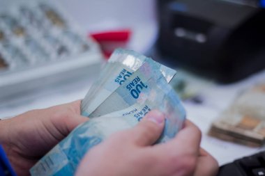 Değişim bürosu / bankada çalışan iş adamının insan eli. O para sayıyor ve bir müşteriye nakit para veriyor. Brezilya Reais 100 reais.