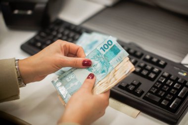 Değişim bürosu / bankada çalışan iş adamının insan eli. O para sayıyor ve bir müşteriye nakit para veriyor. Brezilyalı Reais.