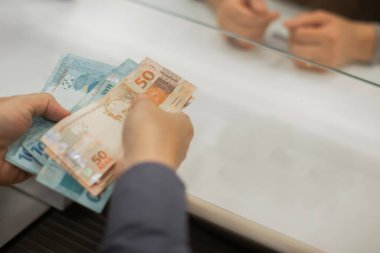 Değişim bürosu / bankada çalışan iş adamının insan eli. O para sayıyor ve bir müşteriye nakit para veriyor. Brezilyalı Reais.