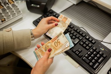 Değişim bürosu / bankada çalışan iş adamının insan eli. O para sayıyor ve bir müşteriye nakit para veriyor. Brezilyalı Reais.