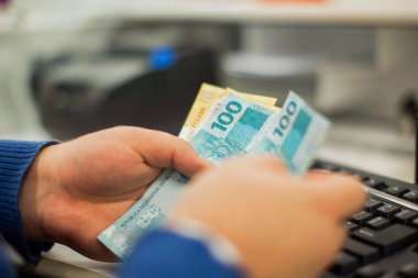 Değişim bürosu / bankada çalışan iş adamının insan eli. O para sayıyor ve bir müşteriye nakit para veriyor. Brezilya Reais 100 reais.