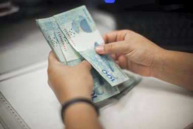 Değişim bürosu / bankada çalışan iş adamının insan eli. O para sayıyor ve bir müşteriye nakit para veriyor. Brezilya Reais 100 reais.