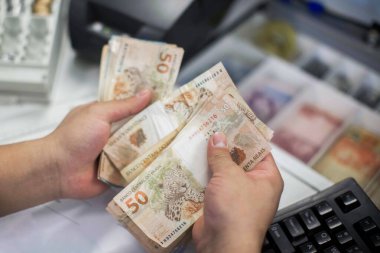 Değişim bürosu / bankada çalışan iş adamının insan eli. O para sayıyor ve bir müşteriye nakit para veriyor. Brezilyalı 50 reais fatura.
