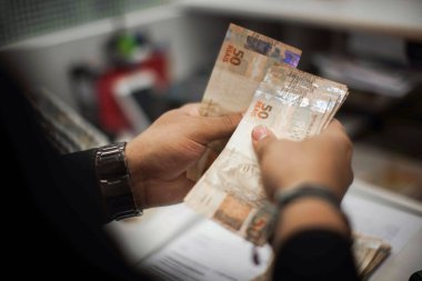 Değişim bürosu / bankada çalışan iş adamının insan eli. O para sayıyor ve bir müşteriye nakit para veriyor. Brezilyalı 50 reais fatura.
