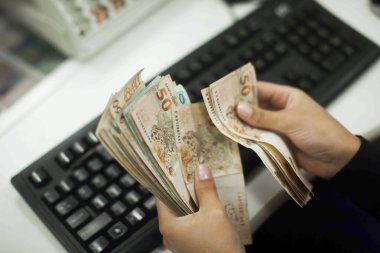 Değişim bürosu / bankada çalışan iş adamının insan eli. O para sayıyor ve bir müşteriye nakit para veriyor. Brezilyalı Reais.