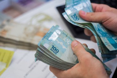 Değişim bürosu / bankada çalışan iş adamının insan eli. O para sayıyor ve bir müşteriye nakit para veriyor. Brezilya Reais 100 reais.