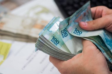 Değişim bürosu / bankada çalışan iş adamının insan eli. O para sayıyor ve bir müşteriye nakit para veriyor. Brezilya Reais 100 reais.