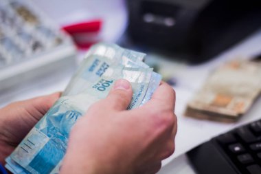 Değişim bürosu / bankada çalışan iş adamının insan eli. O para sayıyor ve bir müşteriye nakit para veriyor. Brezilya Reais 100 reais.