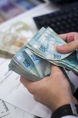 Değişim bürosu / bankada çalışan iş adamının insan eli. O para sayıyor ve bir müşteriye nakit para veriyor. Brezilya Reais 100 reais.