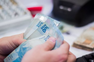 Değişim bürosu / bankada çalışan iş adamının insan eli. O para sayıyor ve bir müşteriye nakit para veriyor. Brezilya Reais 100 reais.