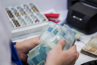 Değişim bürosu / bankada çalışan iş adamının insan eli. O para sayıyor ve bir müşteriye nakit para veriyor. Brezilya Reais 100 reais.