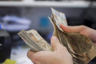 Değişim bürosu / bankada çalışan iş adamının insan eli. O para sayıyor ve bir müşteriye nakit para veriyor. Brezilyalı 50 reais fatura.