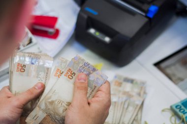 Değişim bürosu / bankada çalışan iş adamının insan eli. O para sayıyor ve bir müşteriye nakit para veriyor. Brezilyalı 50 reais fatura.