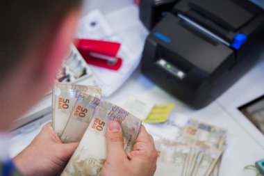 Değişim bürosu / bankada çalışan iş adamının insan eli. O para sayıyor ve bir müşteriye nakit para veriyor. Brezilyalı 50 reais fatura.