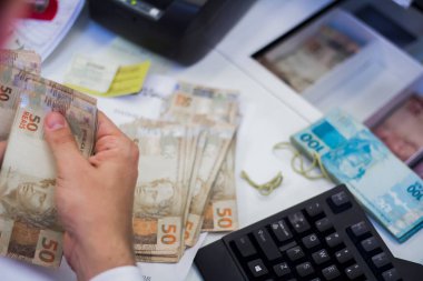 Değişim bürosu / bankada çalışan iş adamının insan eli. O para sayıyor ve bir müşteriye nakit para veriyor. Brezilyalı Reais.