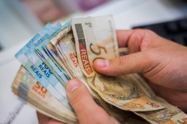 Değişim bürosu / bankada çalışan iş adamının insan eli. O para sayıyor ve bir müşteriye nakit para veriyor. Brezilyalı Reais.