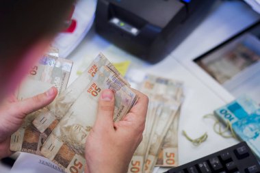 Değişim bürosu / bankada çalışan iş adamının insan eli. O para sayıyor ve bir müşteriye nakit para veriyor. Brezilyalı 50 reais fatura.