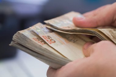 Değişim bürosu / bankada çalışan iş adamının insan eli. O para sayıyor ve bir müşteriye nakit para veriyor. Brezilyalı 50 reais fatura.