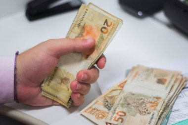 Değişim bürosu / bankada çalışan iş adamının insan eli. O para sayıyor ve bir müşteriye nakit para veriyor. Brezilyalı 50 reais fatura.