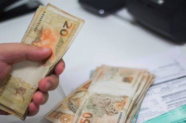 Değişim bürosu / bankada çalışan iş adamının insan eli. O para sayıyor ve bir müşteriye nakit para veriyor. Brezilyalı 50 reais fatura.