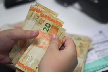 Değişim bürosu / bankada çalışan iş adamının insan eli. O para sayıyor ve bir müşteriye nakit para veriyor. Brezilya Reais - 20 reais fatura.