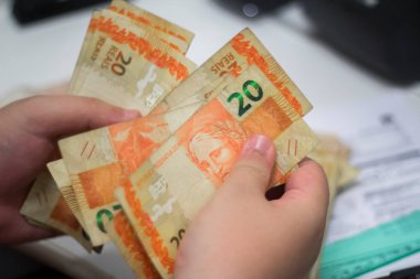 Değişim bürosu / bankada çalışan iş adamının insan eli. O para sayıyor ve bir müşteriye nakit para veriyor. Brezilya Reais - 20 reais fatura.