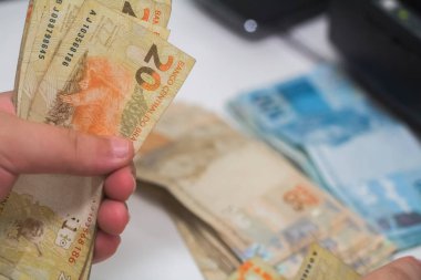 Değişim bürosu / bankada çalışan iş adamının insan eli. O para sayıyor ve bir müşteriye nakit para veriyor. Brezilya Reais - 20 reais fatura.
