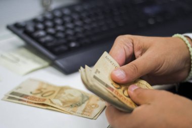 Değişim bürosu / bankada çalışan iş adamının insan eli. O para sayıyor ve bir müşteriye nakit para veriyor. Brezilyalı 50 reais fatura.