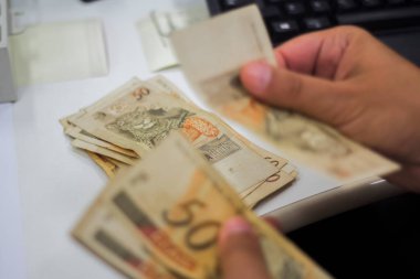 Değişim bürosu / bankada çalışan iş adamının insan eli. O para sayıyor ve bir müşteriye nakit para veriyor. Brezilyalı 50 reais fatura.